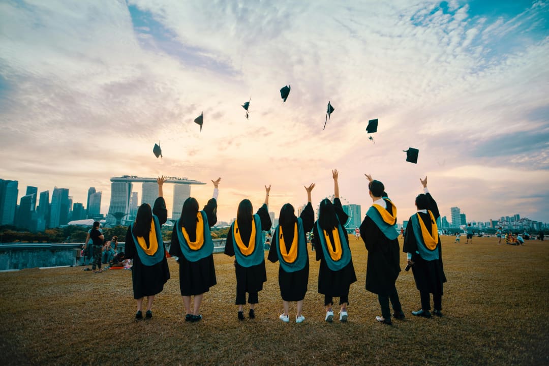 A group of young graduates seen from behind, throwing their caps at sunset.